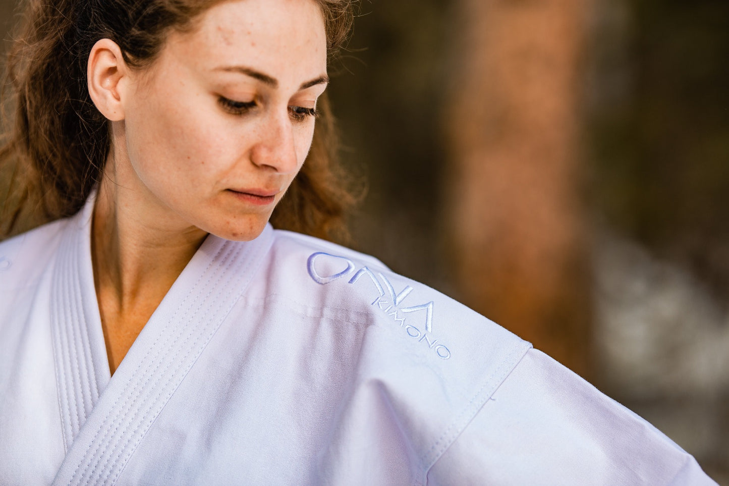Woman looking down at text Onna Kimono embroidered at karate uniform shoulder.