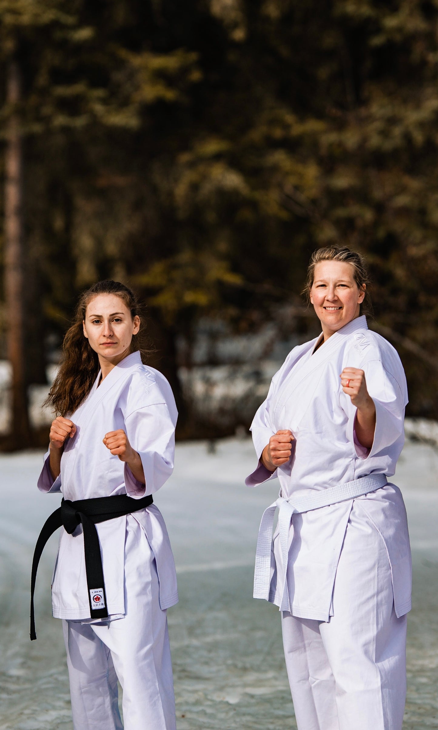 2 women in karate uniforms standing in the snow ready to fight