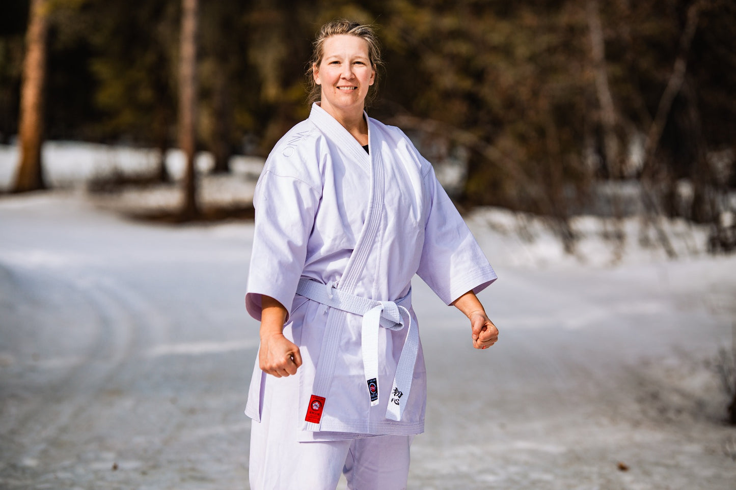 Strong female in white belt and karate uniform standing in the snow